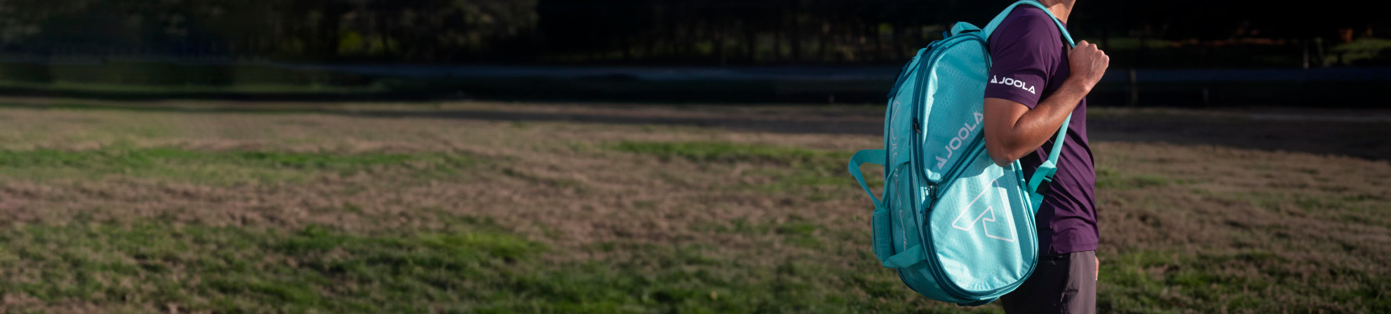 Horizontal banner image of someone posing with a teal JOOLA backpack over their shoulder.